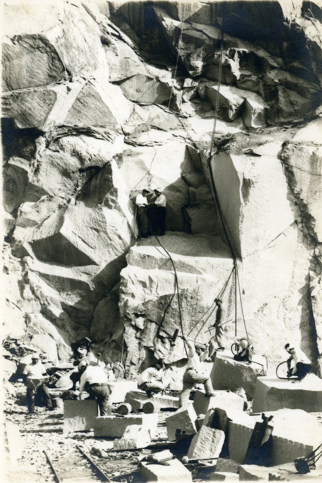 Historical photograph of stoneworkers quarrying beneath a rock face